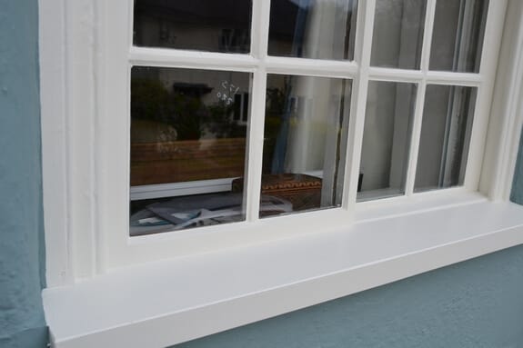 Close-up of a repainted white window sill and glazing bars against blue-grey render