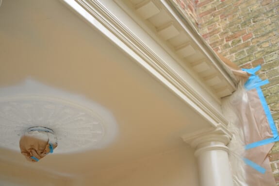 Porch ceiling being painted around a ceiling rose, the light fitting wrapped in paper and blue tape