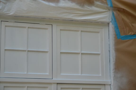 Close-up of casements sprayed white with masked panes, plastic sheeting above and taped masking paper beside