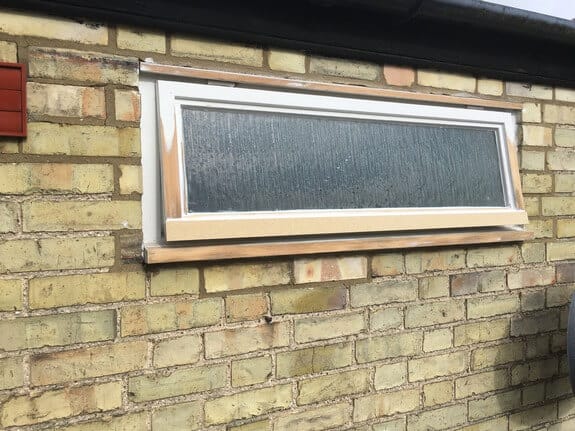 Small obscure-glazed window in yellow brick with its frame and sill in bare, unpainted timber