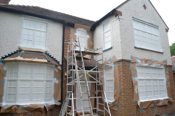House front with a bay and casement windows masked in brown paper and blue tape, scaffold tower in the centre