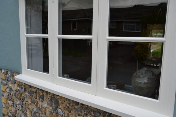 Freshly painted white timber window and sill in blue render above flint walling