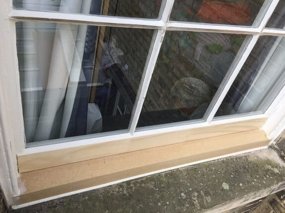 Base of a multi-pane timber window with new, unpainted timber on the bottom rail and sill