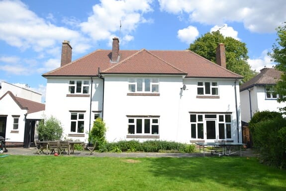 Large white-rendered detached house with a hipped clay-tiled roof and white timber casement windows, seen across a lawn
