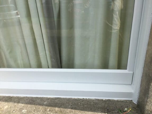 Freshly painted white bottom rail and sill of a timber window, with curtains behind the glass