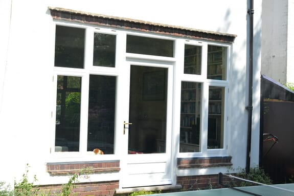 White-painted timber glazed door with flanking casements and top lights in a white-rendered wall above brick sills