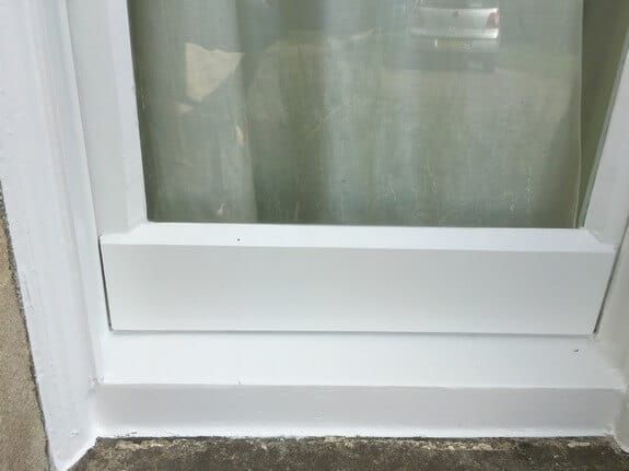 Close-up of the newly painted white bottom rail and sill of a timber window