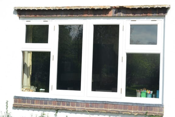 Four-light white timber casement window with top lights, set in white render above a red brick sill course