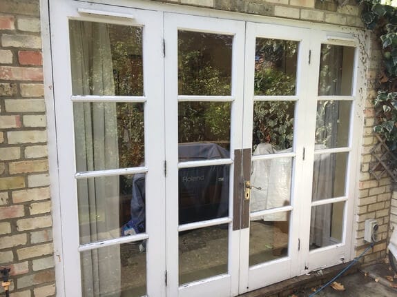 Four-leaf glazed timber patio doors with worn white paint in a yellow brick wall