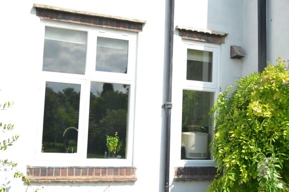 Two white-painted timber casement windows with tiled heads in a white-rendered wall, beside a climbing plant