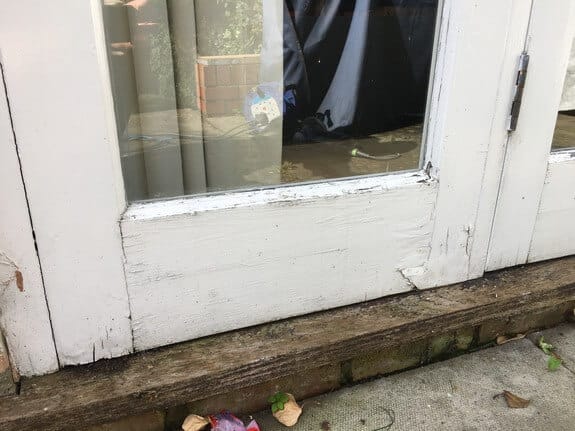 Bottom rail of a timber patio door with dirty, worn paint and a split near the corner joint