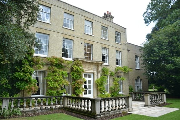 Angled view of the garden front, its white sash windows framed by climbing plants and a stone balustrade