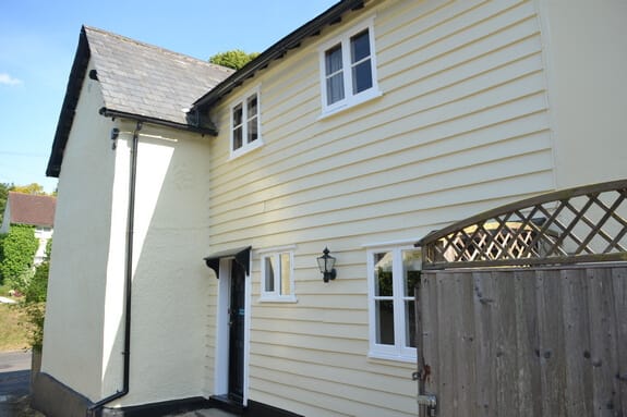 Cream weatherboarded and rendered cottage with white casement windows, black gutters and a slate roof after repainting