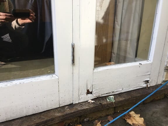 Bottom of two timber patio door leaves with peeling paint and a rotten hole at the base of a stile