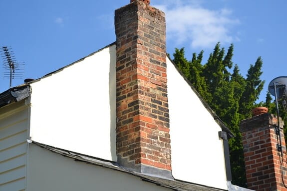 White-painted rendered gable wall with a red brick chimney stack rising through it and a second chimney beyond