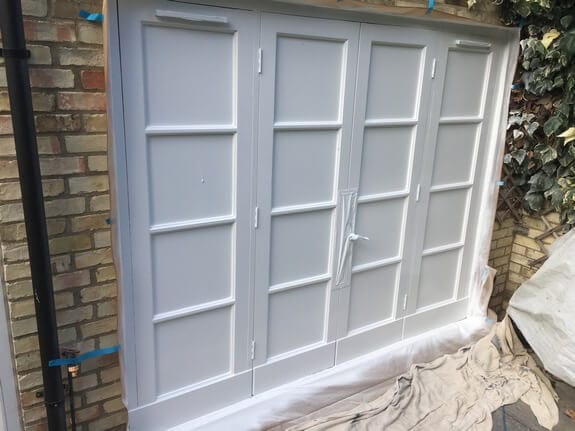 Patio doors sprayed white with the glass masked, blue tape on the brickwork and dust sheets below