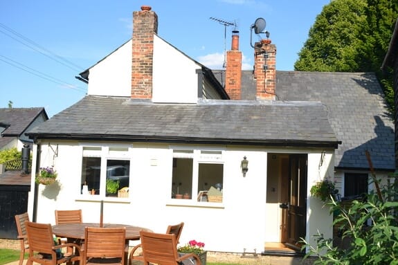 Cottage with white-painted render, white timber casement windows, slate roof and brick chimneys, garden table in front