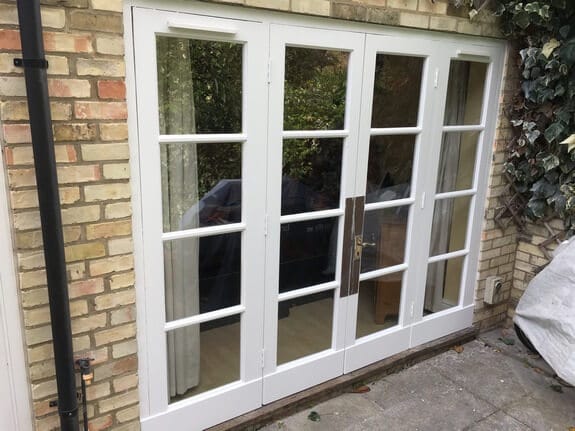 Four-leaf timber patio doors freshly painted white in a yellow brick wall, with ivy alongside