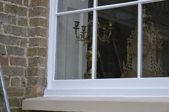 Lower edge of a white-painted sash window and cream sill in pale brickwork, brass ornaments inside