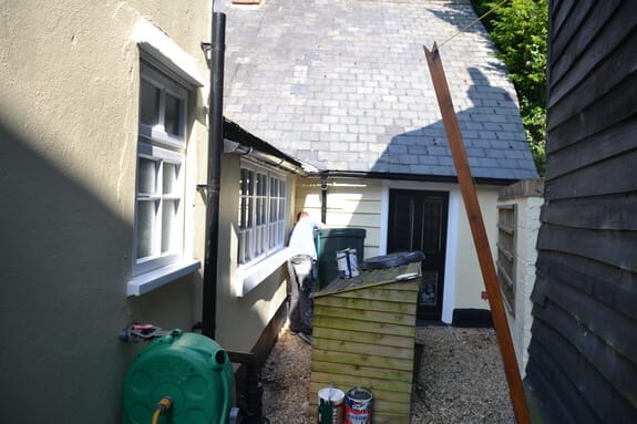 Side passage with white multi-pane casement windows, a black back door and cream weatherboarding under a slate roof
