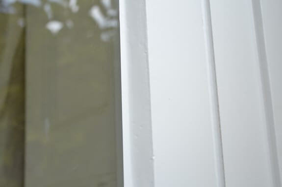 Close-up of smooth white paint on a window frame and beading beside the glass