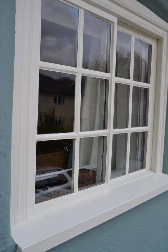 Multi-pane timber window and sill repainted off-white, set in a blue-grey rendered wall