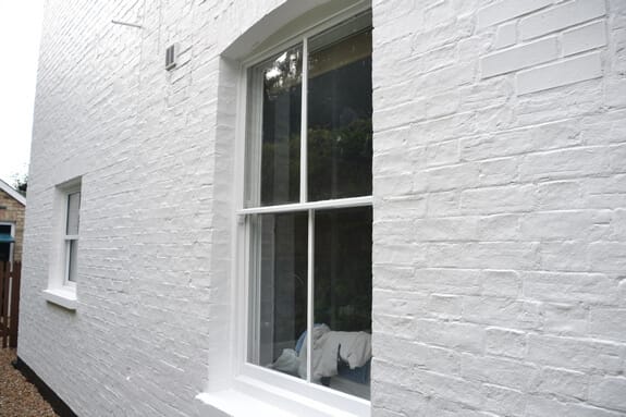 Two-over-two white sash window in a white-painted brick wall