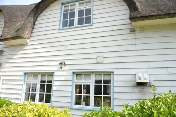 White weatherboarded thatched cottage with blue-framed timber casement windows