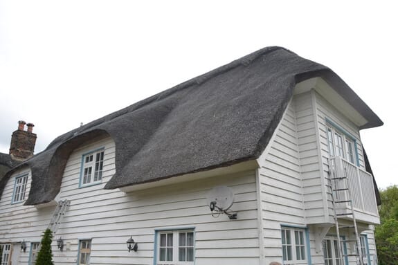 Thatched house clad in white weatherboarding, with blue-framed windows and a ladder against the gable