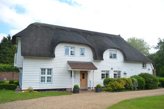 Grade II listed thatched cottage with white weatherboard cladding, eyebrow dormers and a tiled porch