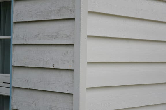 Corner of weatherboard cladding, weathered on one side and freshly painted white on the other