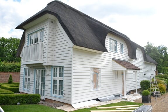 Thatched cottage with a balcony gable, a ladder, a window masked in plastic and dust sheets on the lawn