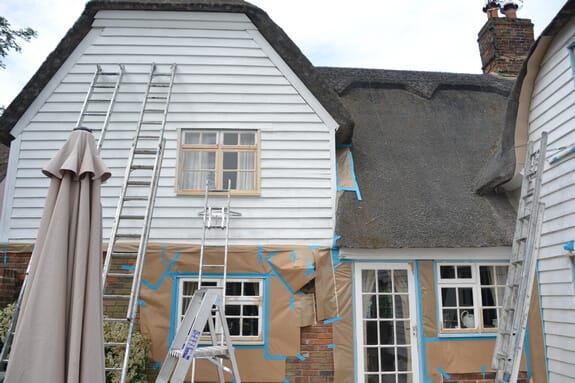 Weatherboarded gable with ladders against it and masking paper taped over the brickwork below