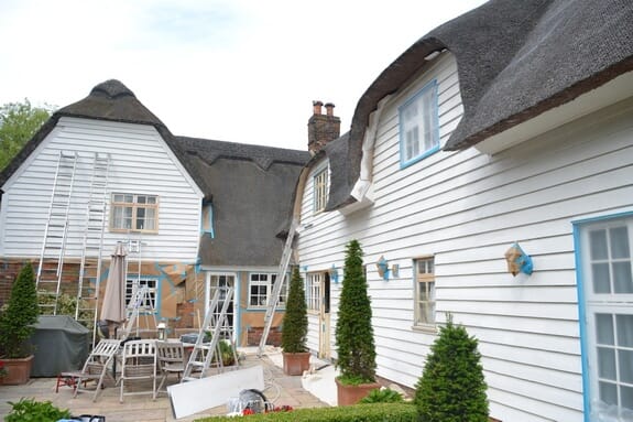Courtyard of the thatched cottage with white weatherboard walls, ladders, topiary and garden furniture