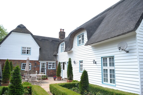 Thatched cottage courtyard with white weatherboarding, pale blue windows and clipped box hedges