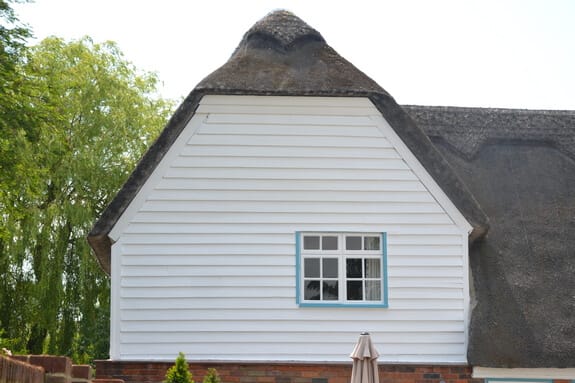Thatched cottage gable with smooth white weatherboarding and a casement window with a pale blue frame