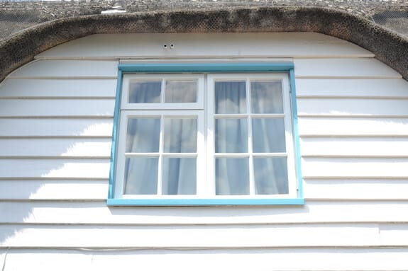Casement window with white frames and a pale blue surround under the thatched eaves