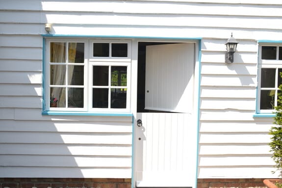 White stable door with its top half open between casement windows with pale blue frames