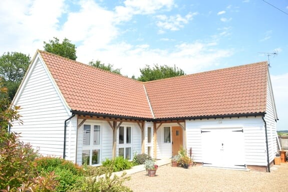 Single-storey white weatherboarded building with a clay-tiled roof, timber-framed porch and gravel drive