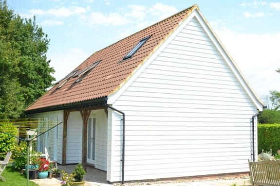 Gable of a white weatherboarded building with a clay-tiled roof, rooflights and a timber-post veranda