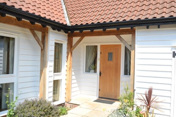 Timber-framed porch with a natural wood front door, white weatherboard walls and a clay-tiled roof