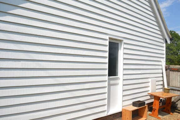 White weatherboard wall with a half-glazed door, a small timber table and a stool