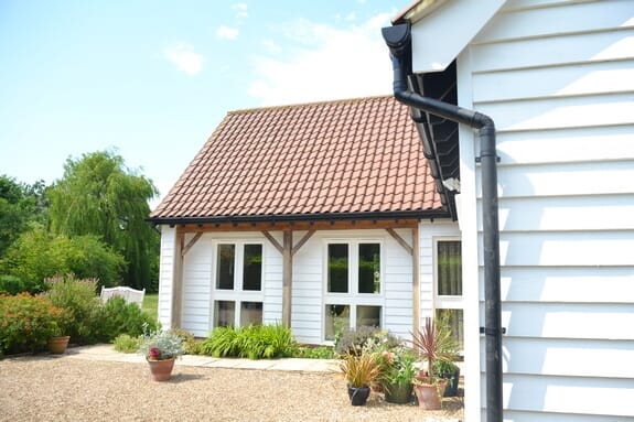 White weatherboarded building with glazed doors between timber posts and a clay-tiled roof beside a gravel yard