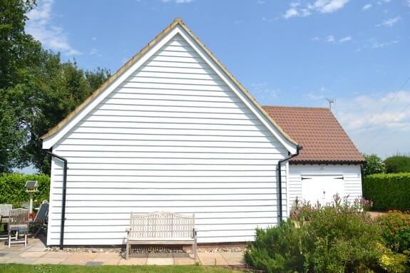 Gable end of a white weatherboarded building with a clay-tiled roof and a garden bench in front