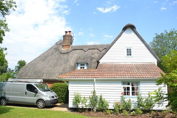 Thatched cottage with a white weatherboarded gable and a clay-tiled single-storey wing, a van parked alongside