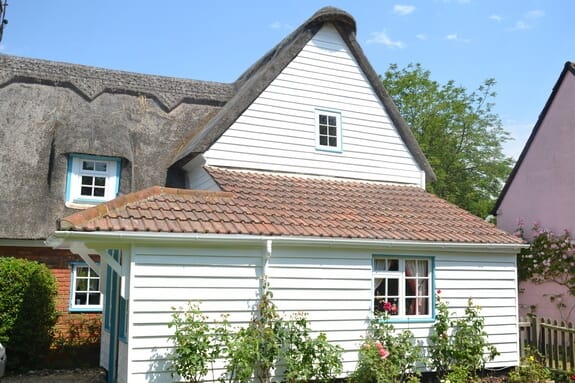 White weatherboarded gable and clay-tiled single-storey wing of a thatched cottage, with pale blue windows