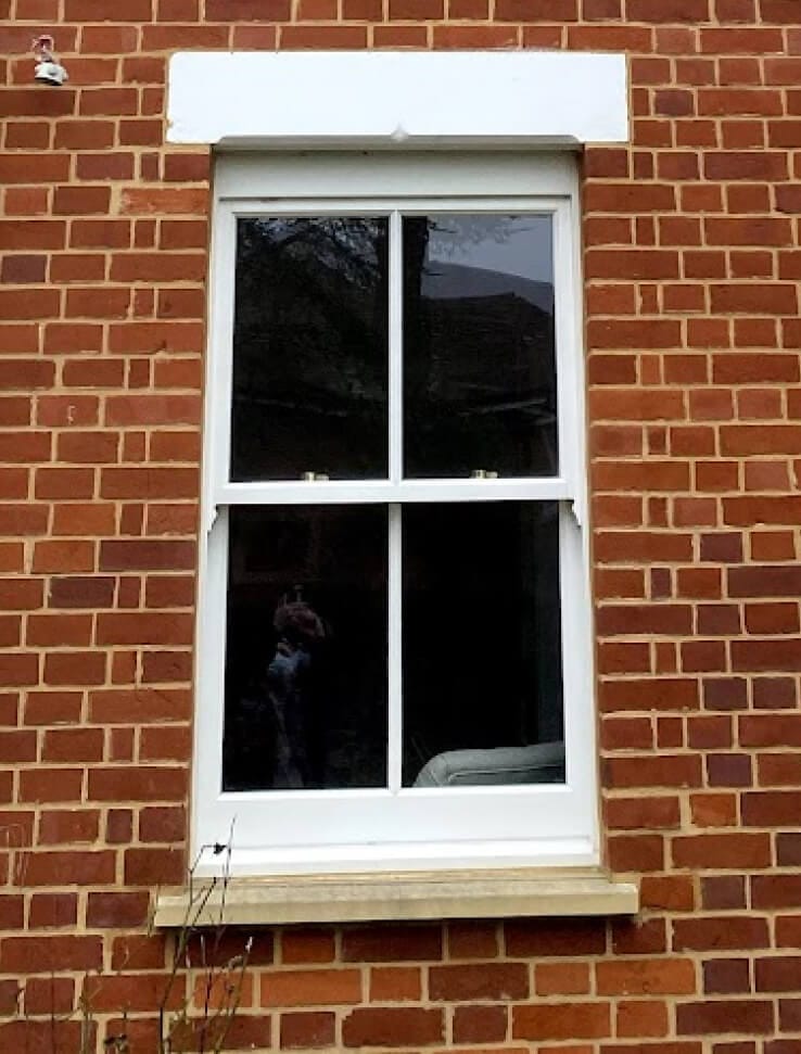 A white two-over-two sash window with a centre bar in a red-brick wall