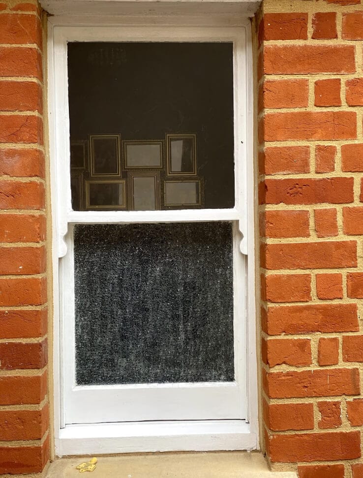 A one-over-one sash window with horns, obscured glass in the lower sash, in an orange brick wall