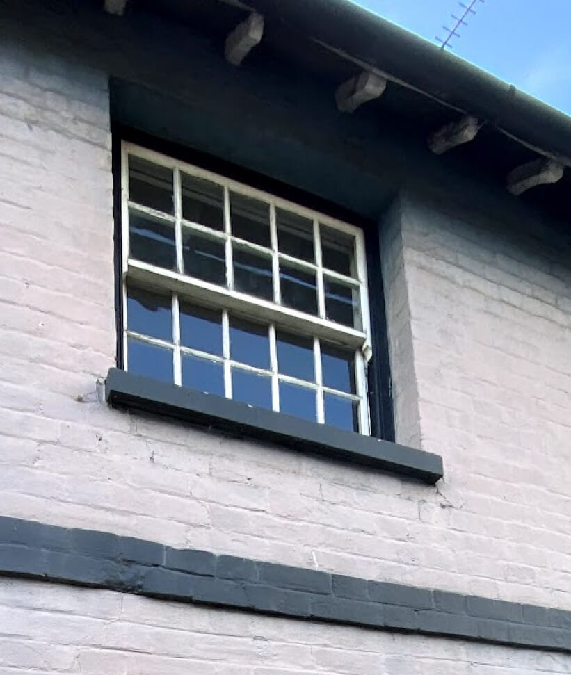 A small sash window with ten panes in each sash under the eaves of a painted brick house