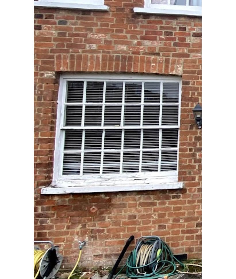 A wide sash window with twelve panes in each sash in a red-brick wall